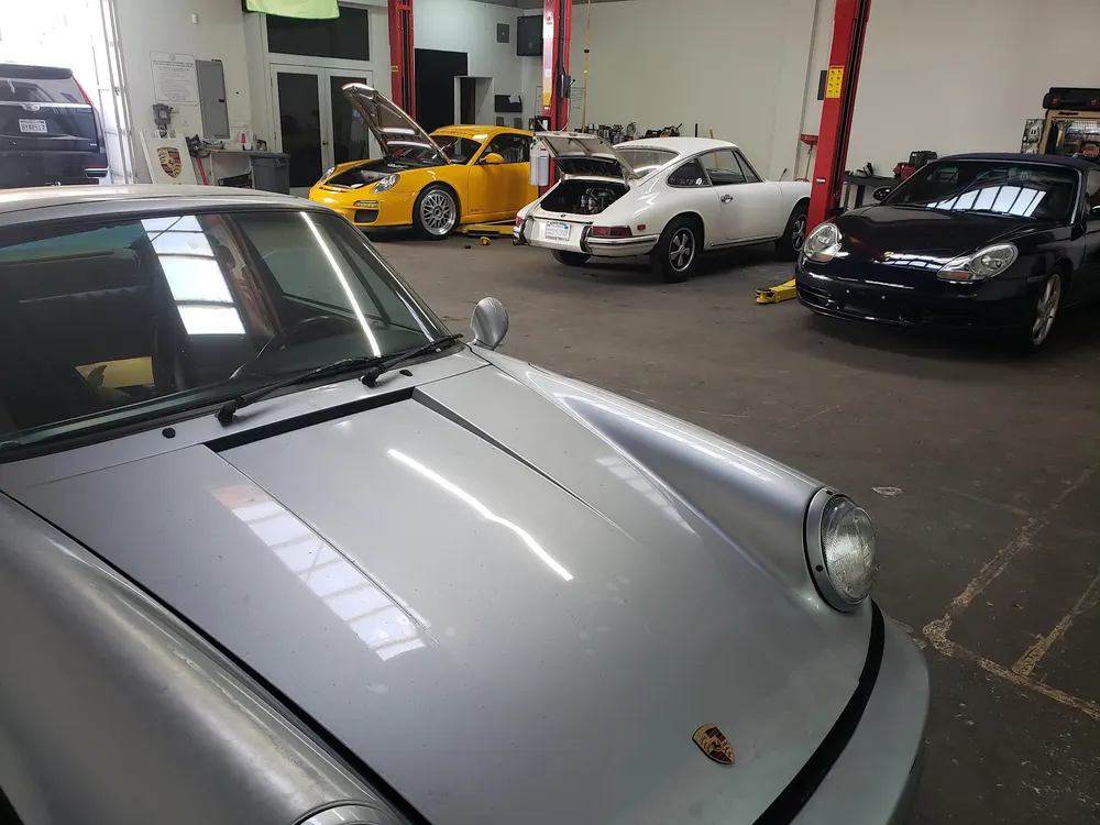 Silver air-cooled Porsche 911 in the foreground with yellow and white 911s in the shop behind it