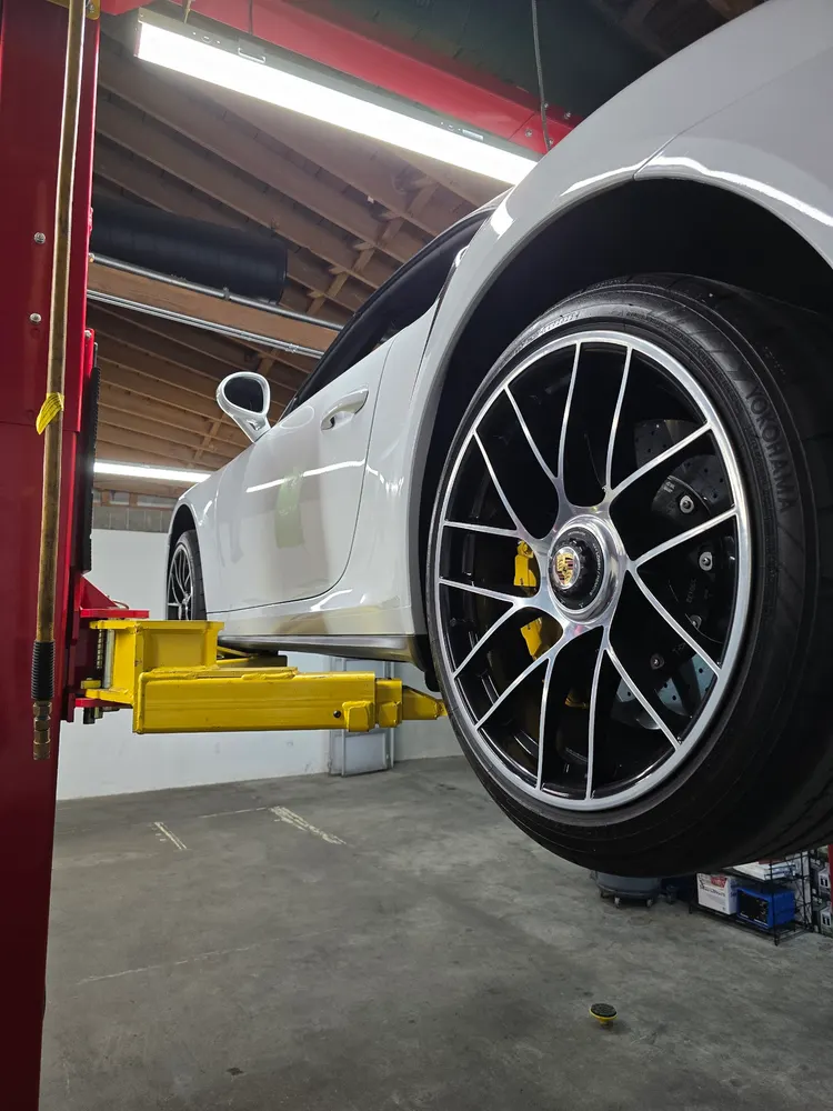Wheel and yellow brake caliper of a white Porsche 911 raised on a lift
