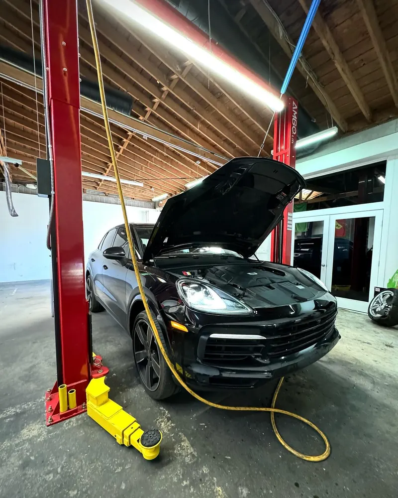 Black Porsche Panamera with the hood open between lift posts