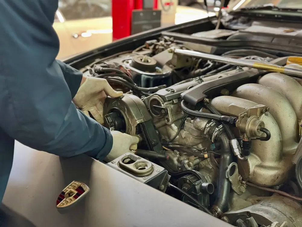 Technician working in the engine bay of a front-engine Porsche