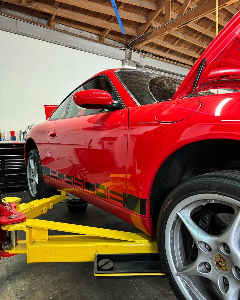 Red Porsche Boxster on lift arms in the shop